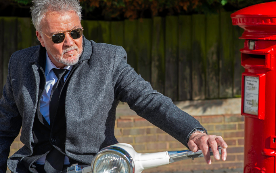 Paul Young Paul Young sat on a Vespa scooter wearing shades and a suit by a red post box