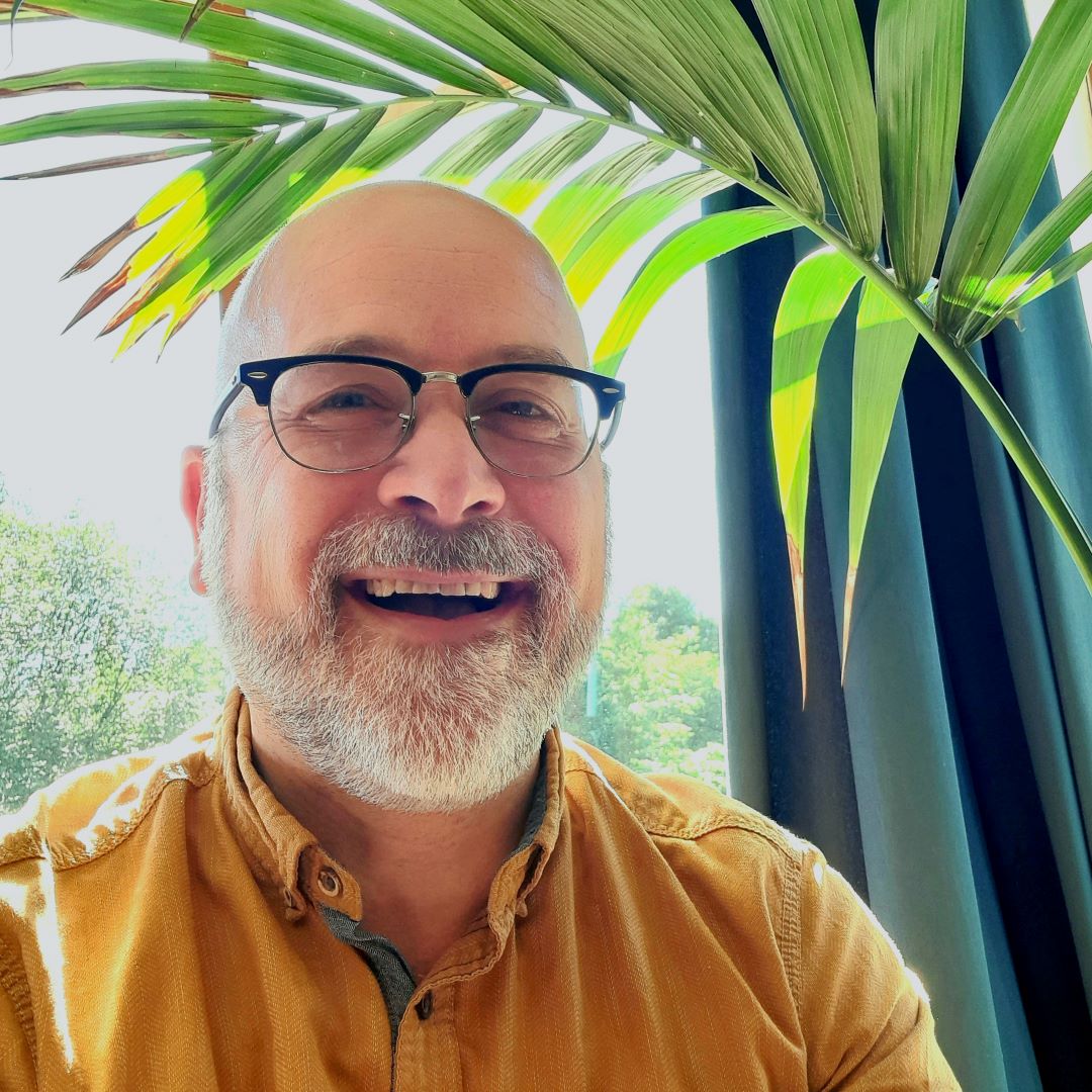 Robb Barham 1080x1080 Robb Barham in glasses and an orange shirt with a green plant behind